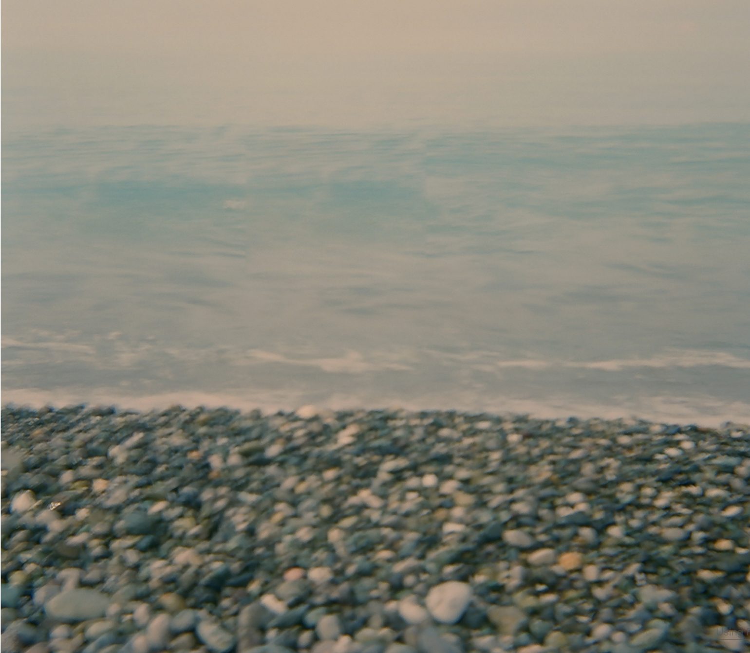 A pebble shore meeting calm, pale sea